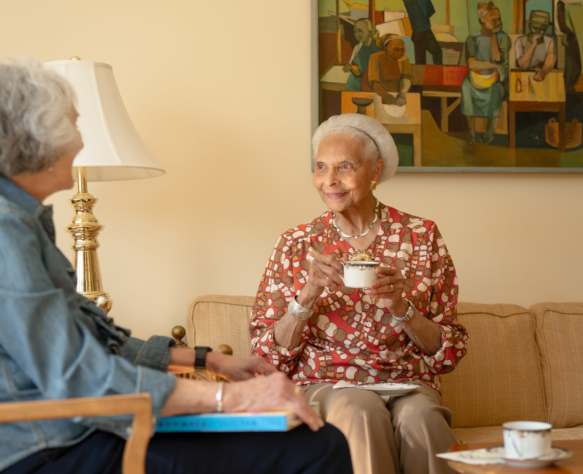 A woman talking with another woman holding a teacup. 